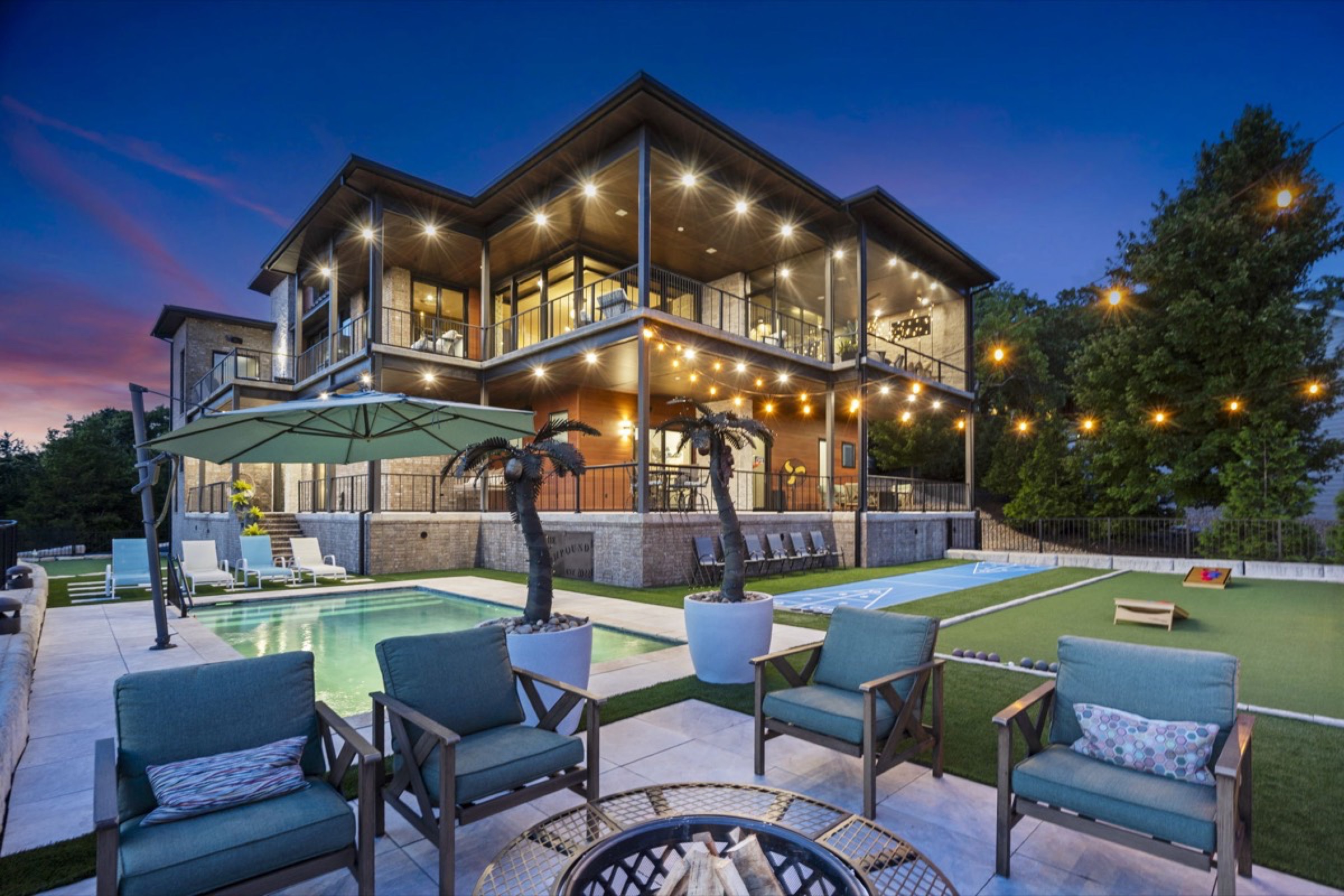 Premium short-term rental at twilight with pool, fire pit, and string lights
