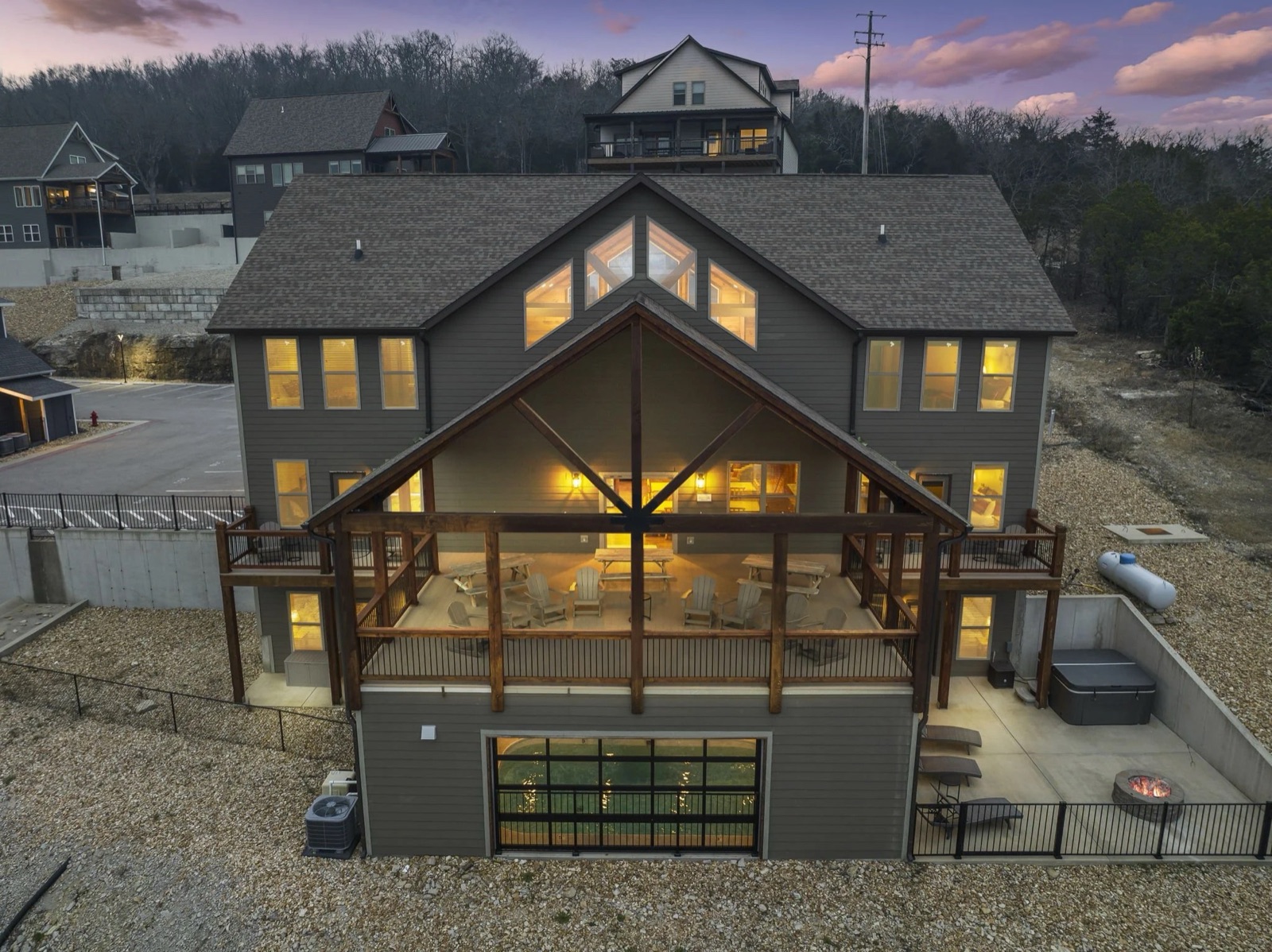 Drone twilight of luxury three-story Branson STR with glowing windows and hot tub